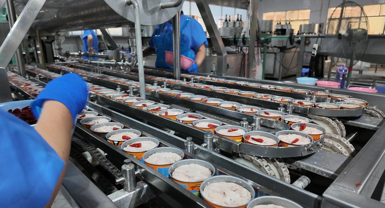 Chili added to open tuna cans by hand on the line